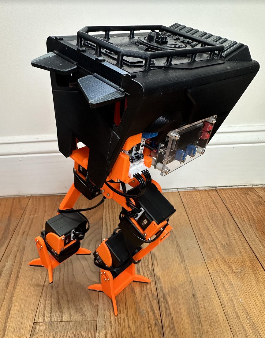 The real robot mid-stride on a wood floor, one leg lifted and swinging forward.